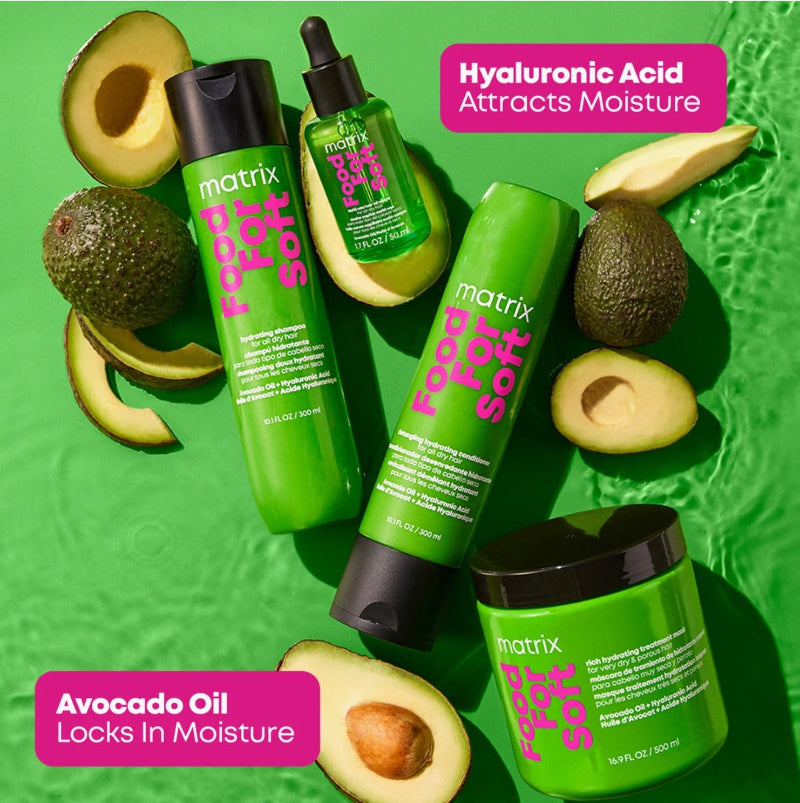 Four green Matrix hair care products arranged on a bright green textured background with sliced avocados around them. Text callouts read 'Hyaluronic Acid Attracts Moisture' and 'Avocado Oil Locks in Moisture.