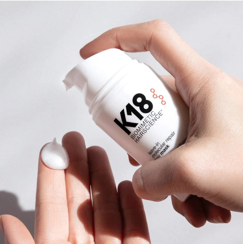 Hand holding a K18 skincare product with a white background