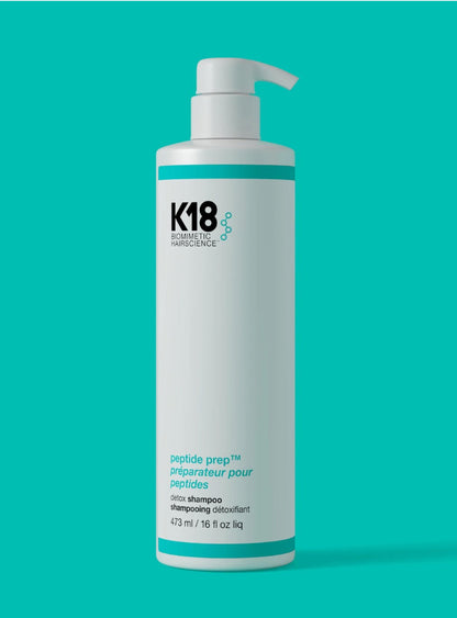 A white bottle of K18 Cosmeceutical Science peptide prep shampoo 16 oz with a white pump dispenser, set against a solid teal background.