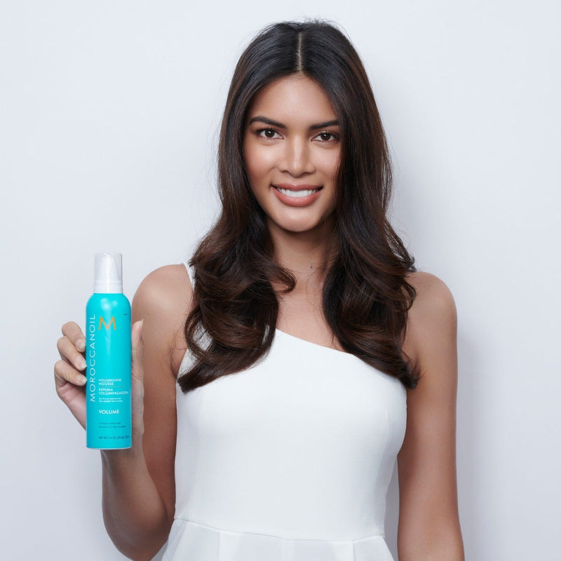 Woman holding a volumizing Moroccanoil hair product bottle against a white background