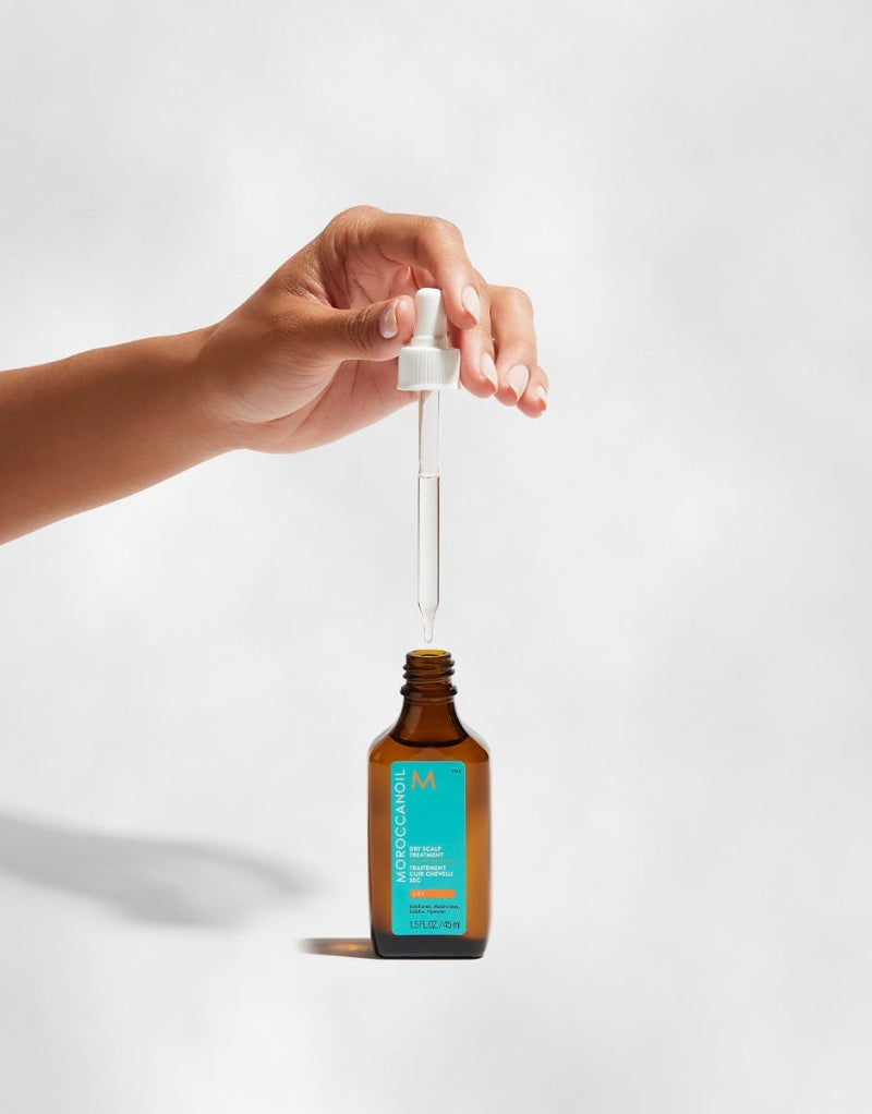Hand holding a dropper over a bottle with a white background. the product belongs to Moroccanoil dry scalp treatment