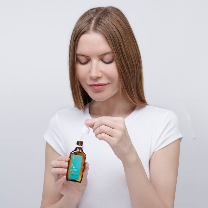 Woman holding a small bottle with a dropper against a plain background showing application of Morrocanoil dry scalp treatment