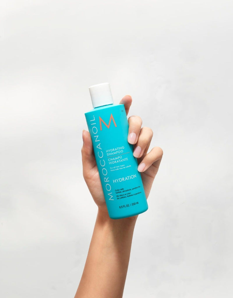 Hand holding a blue shampoo bottle with white cap on a light gray background