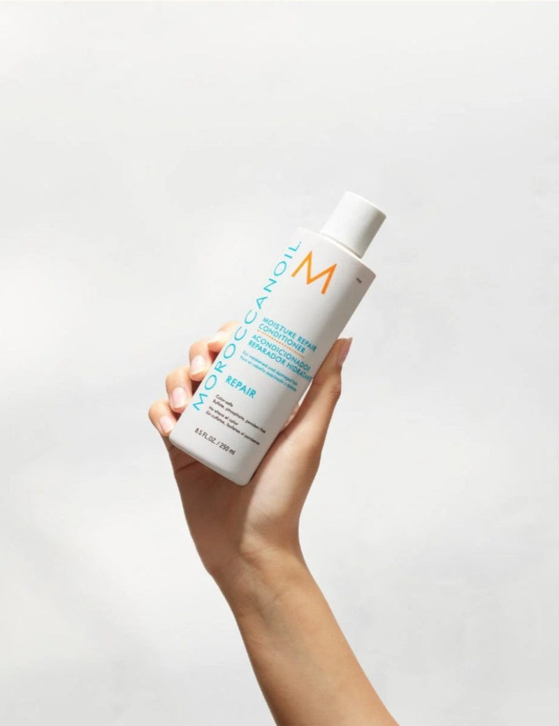 Hand holding a bottle of Moroccanoil product against a light gray background