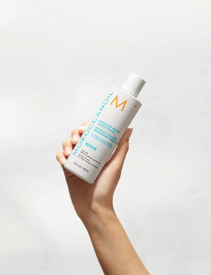 Hand holding a bottle of Moroccanoil product against a light gray background