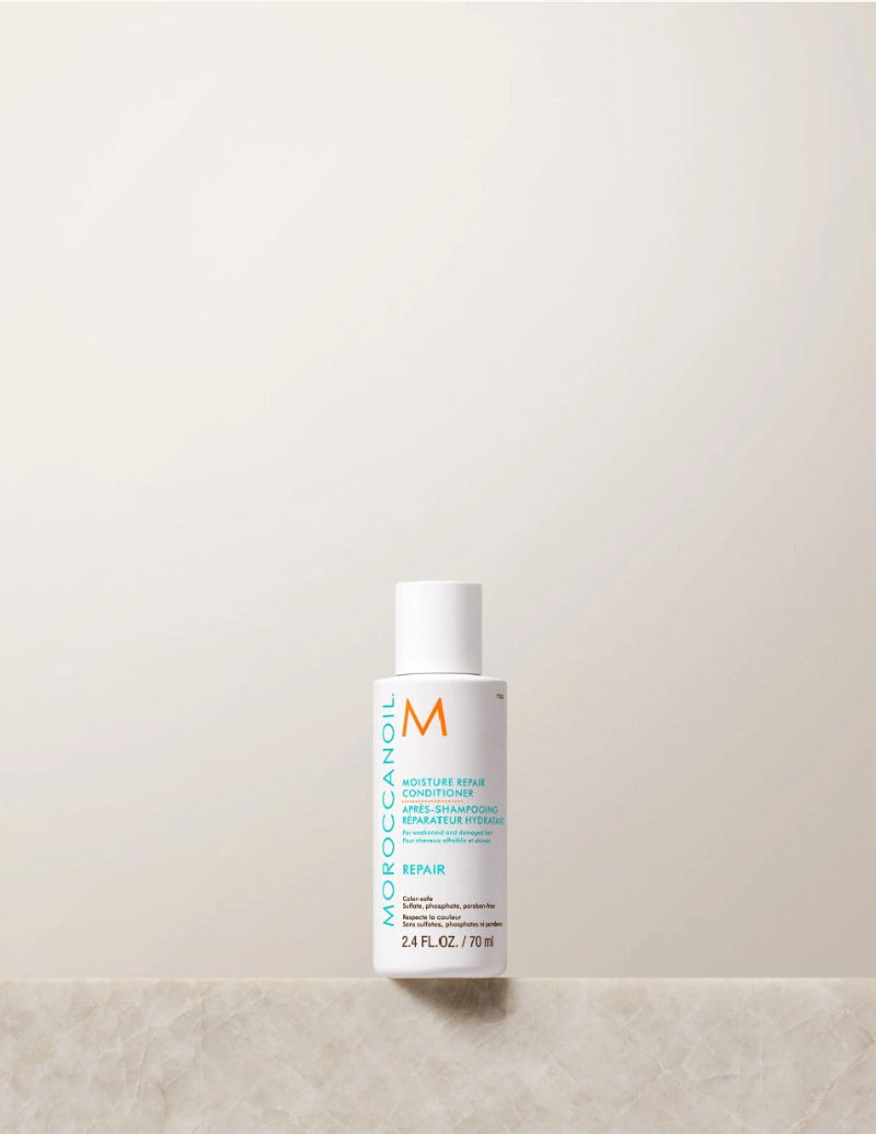 Moroccanoil Moisture Repair Conditioner bottle travel size standing on a light marble surface against a warm off-white background.
