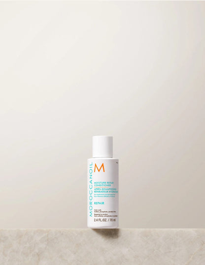 Moroccanoil Moisture Repair Conditioner bottle travel size standing on a light marble surface against a warm off-white background.