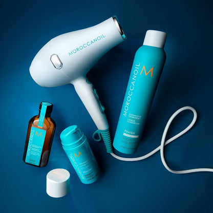 Moroccanoil hair care set arranged on a dark blue background, including a white hair dryer, a turquoise styling foam can and other products for the best hair volume result