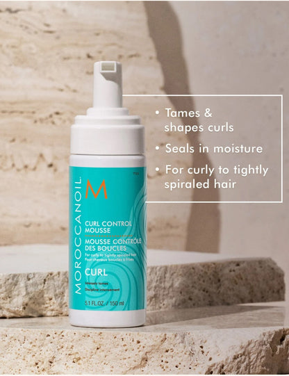 Moroccanoil Curl Control Mousse bottle on a textured stone surface with a text overlay detailing product benefits.