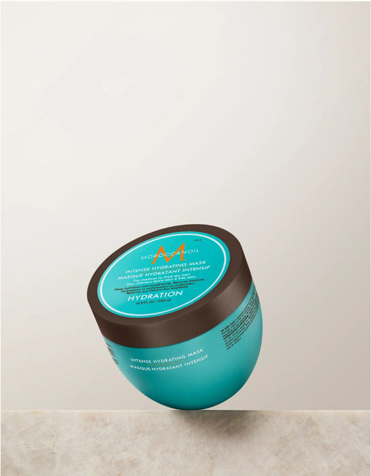 A jar of Moroccanoil Intense Hydration Mask in a vibrant teal color with a dark brown lid, shown floating against a light beige background.
