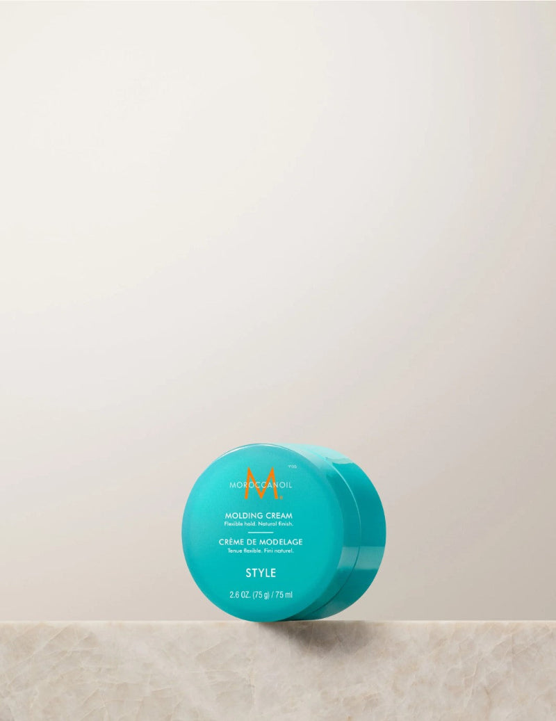 A turquoise blue jar of Morocool Style Molting Cream resting on a light beige marble surface against a warm off-white background.