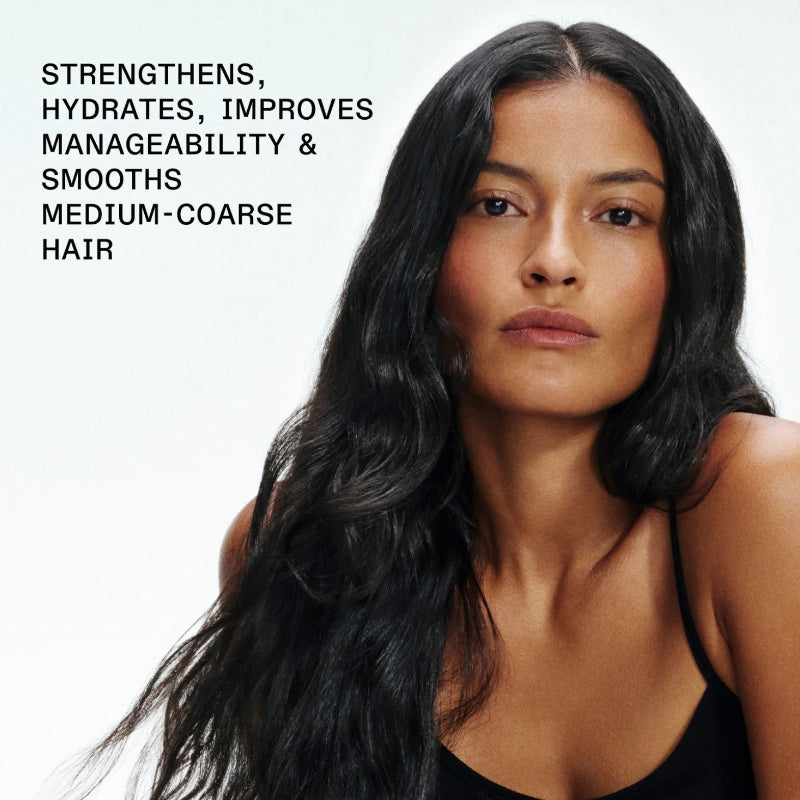 A close-up portrait of a woman with long, dark, wavy hair wearing a black top against a light background, with text on the left stating: 'STRENGTHENS, HYDRATES, IMPROVES MANAGEABILITY & SMOOTHS MEDIUM-COARSE HAIR'. she used Olaplex strengthening shampoo and conditioner