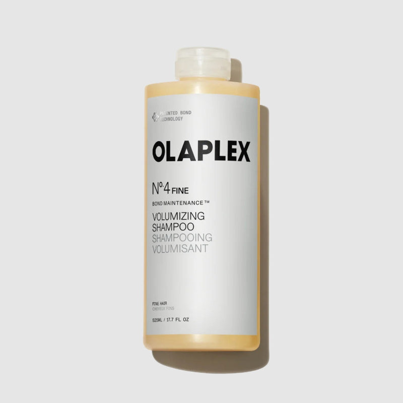 A bottle of Olaplex No.4 Fine Bond Maintenance Volumizing Shampoo, 18oz featuring a white label with black text and a translucent cap, set against a light gray background with a soft shadow.
