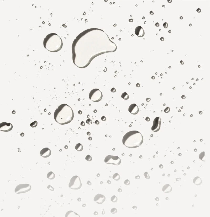 A close-up of Olaplex intensive bond building hair spray droplets and small scattered droplets on a light gray background.
