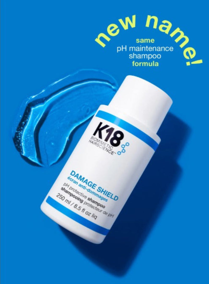 A small white bottle of K18 Damage Shield haircare shampoo with blue text and a blue smear of product on a bright blue background, with yellow text reading 'new name! same pH maintenance shampoo formula.'.